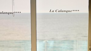 A table with two chairs, a wooden top, and a view of the sea through large windows. - Hôtel La Calanque (Cavalaire-sur-Mer)