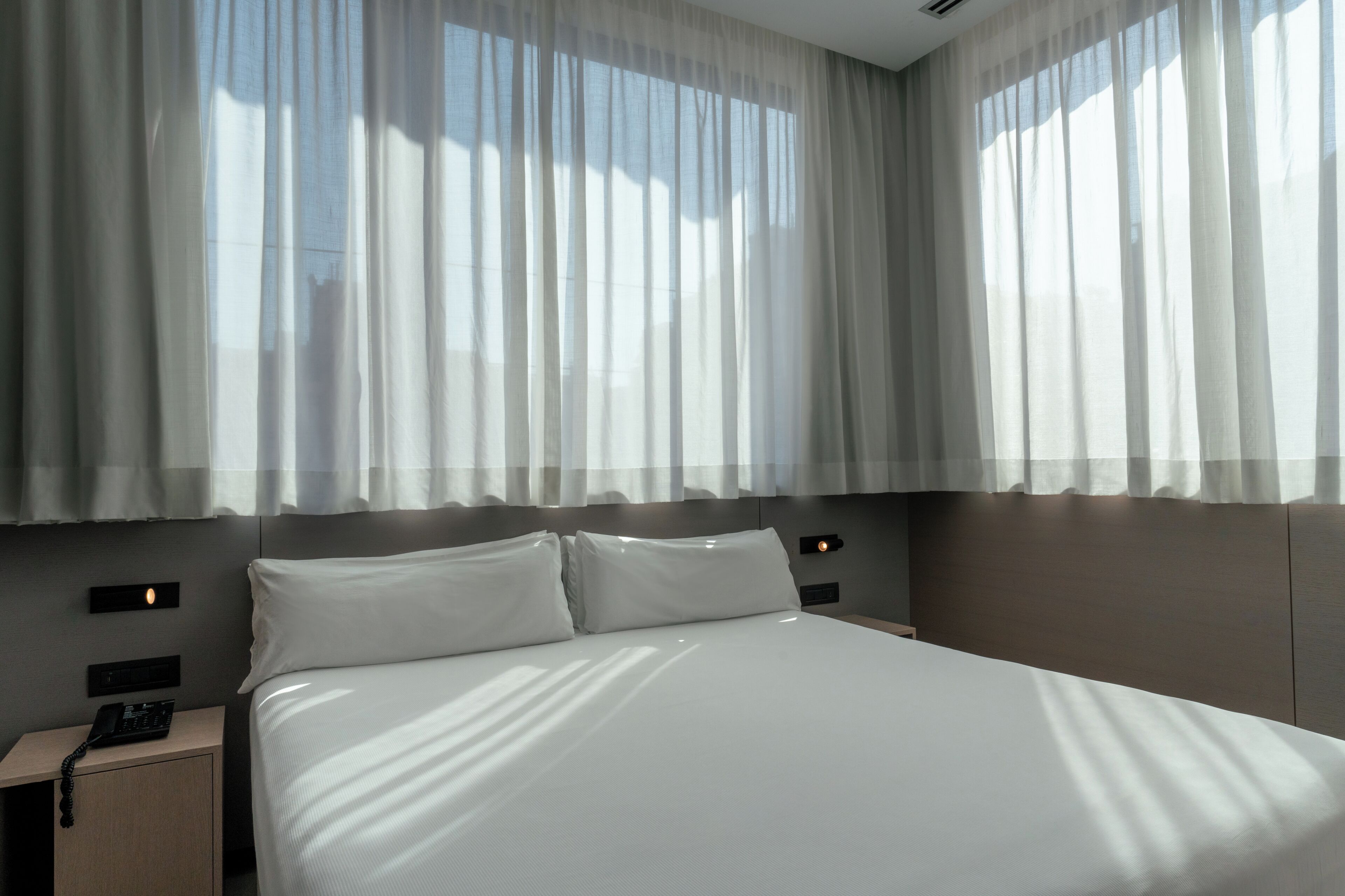 Una habitación de hotel moderna con una cama grande, dos mesitas de noche y una lámpara de pared.