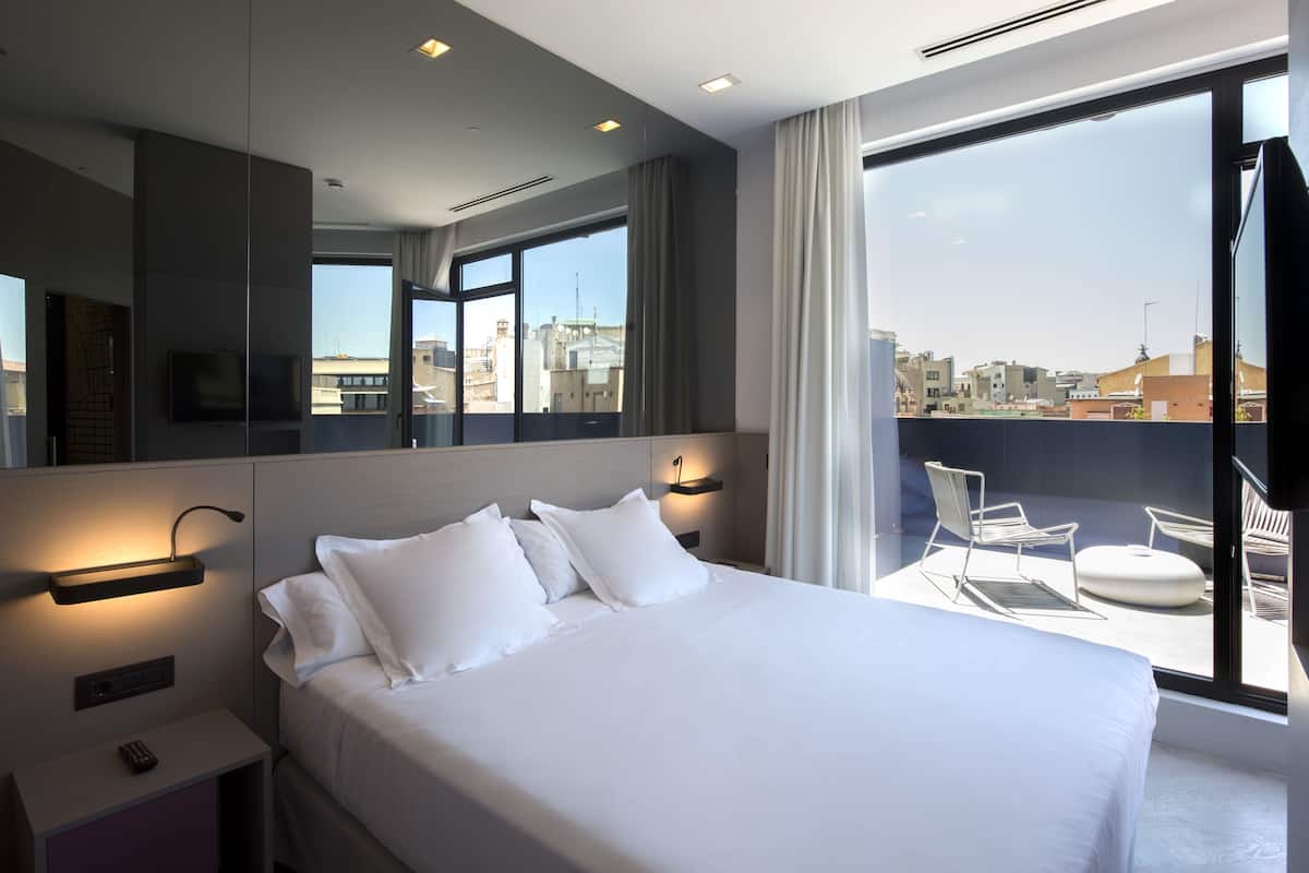 A modern hotel room with a large bed, a TV, and a balcony with seating.