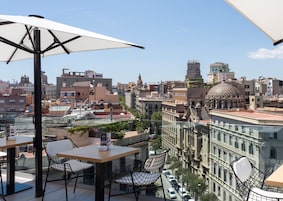 Terraço no telhado com mesas e cadeiras, proporcionando vista para um horizonte urbano com edifícios históricos e uma cúpula imponente.