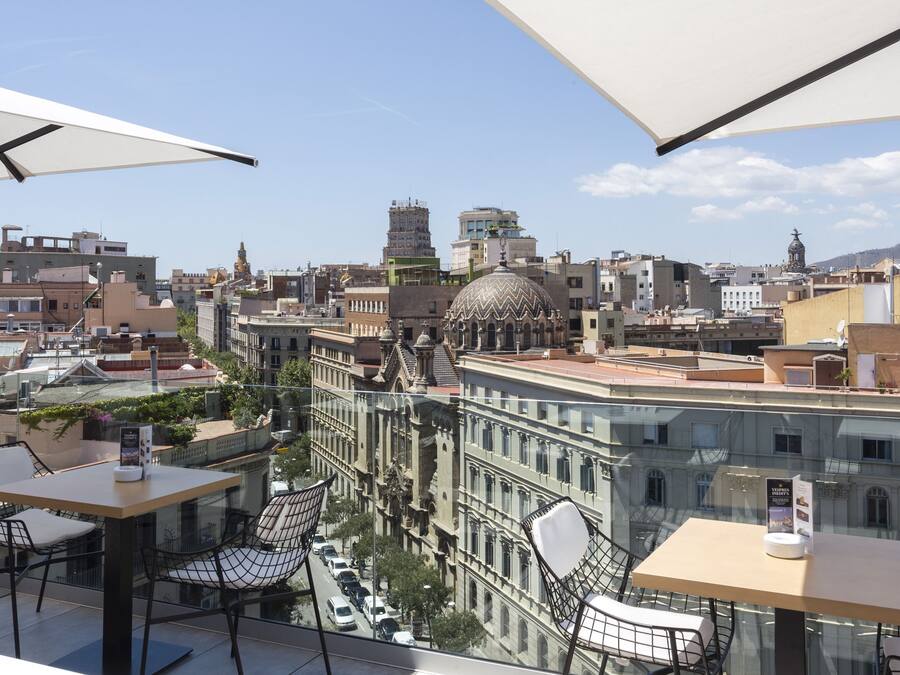 Terraza en la azotea con mesas y sillas, con vistas a un paisaje urbano que incluye edificios históricos y una cúpula destacada.