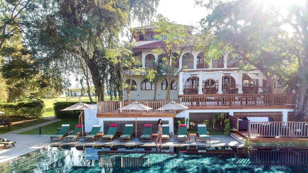 A pool area with lounge chairs and umbrellas, a large building with arched windows, and a well-maintained garden. - Sanctum Inle Resort (Nyaungshwe)