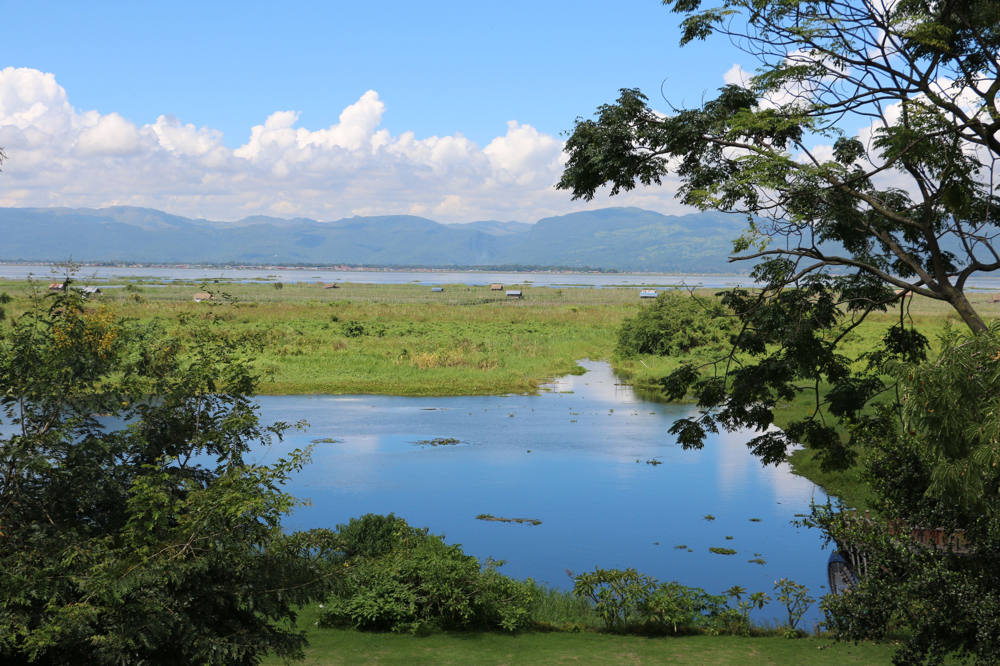 A serene landscape with a calm lake, lush greenery, and distant mountains.