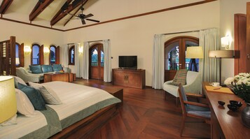 A spacious bedroom with a large bed, a sofa, a television, and a desk with a lamp and flowers.