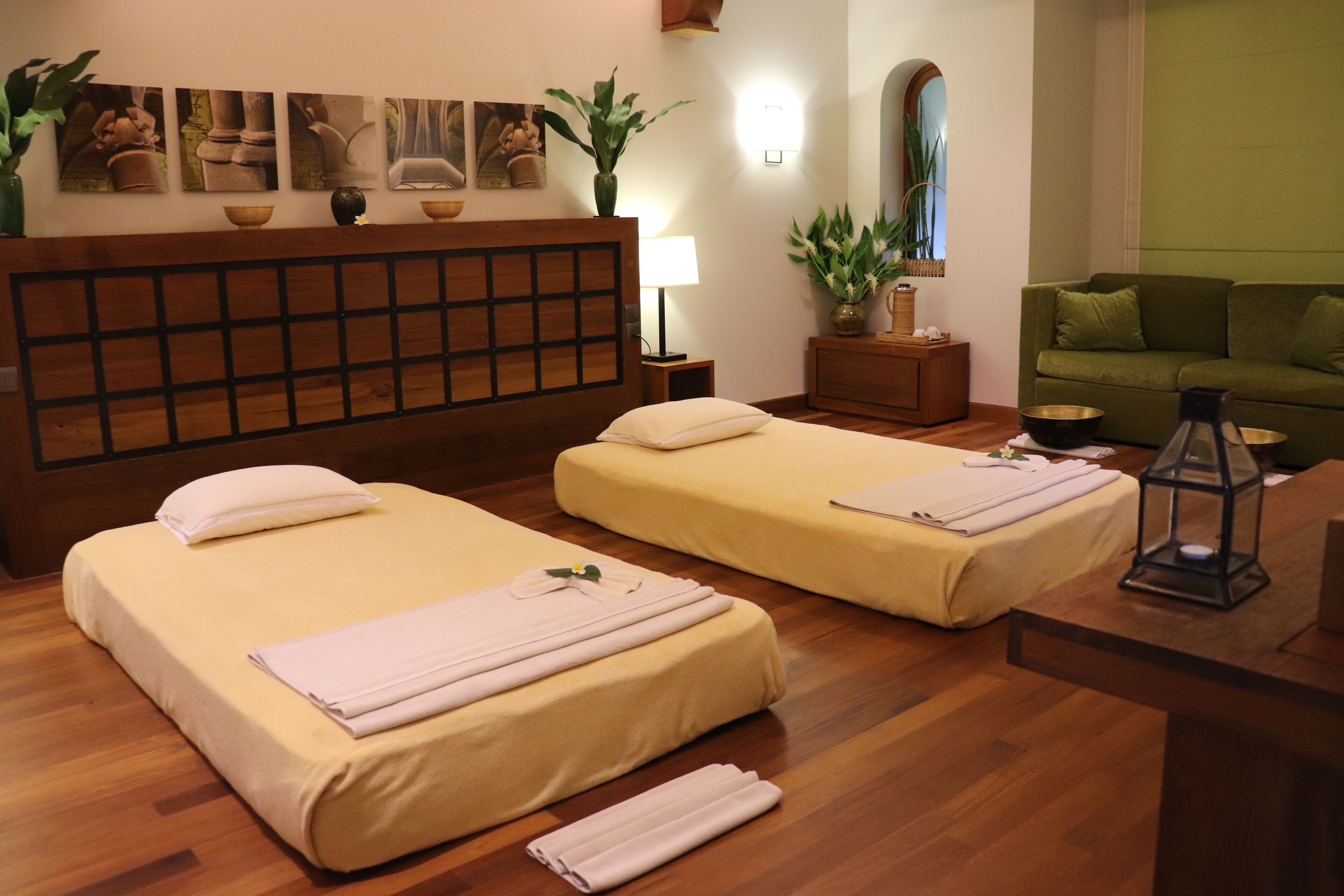 A hotel room with two beds, a wooden headboard, a green couch, a nightstand with a lamp, and a mirror.