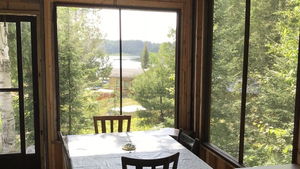 A dining area with a table and chairs, large windows with a view of greenery and a body of water.