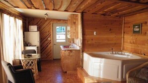 A wooden cabin with a kitchenette, a dining area, and a large bathtub.