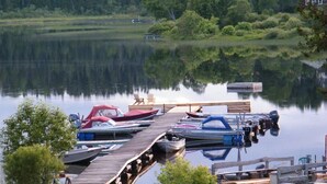 A dock with boats and a wooden pier extending into a calm lake surrounded by greenery.