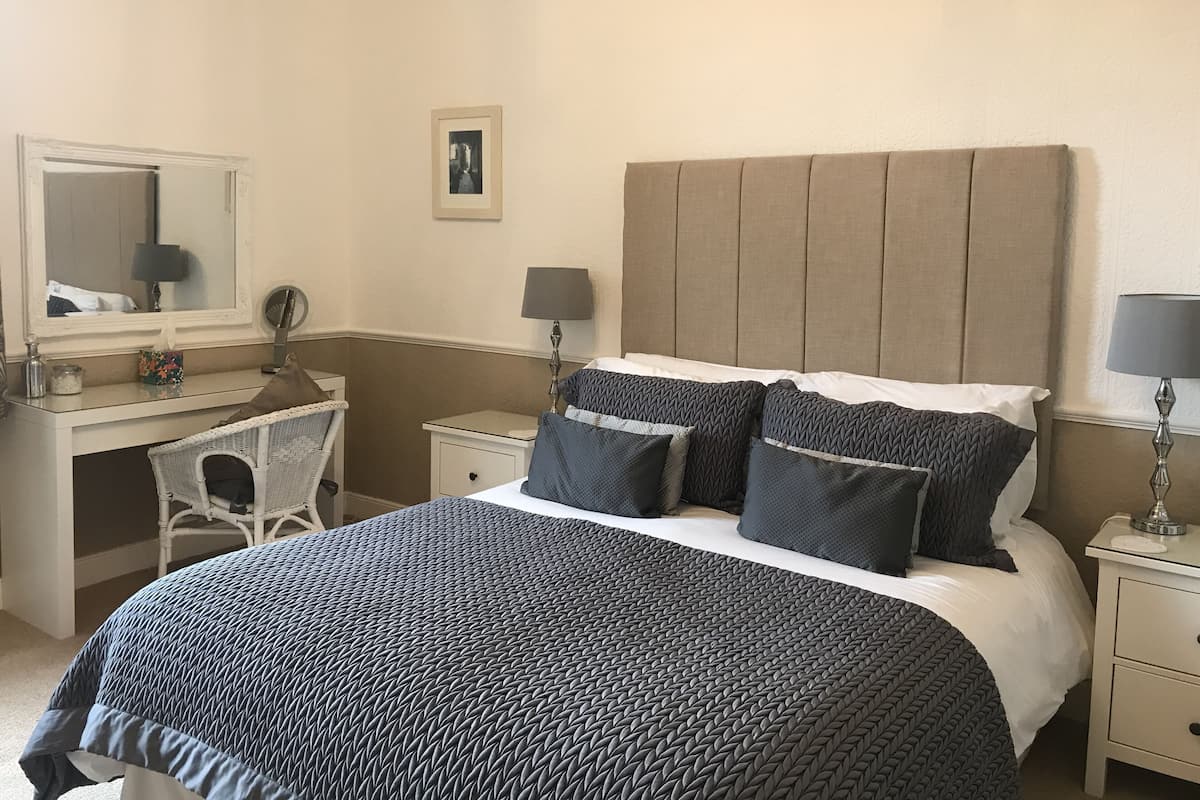 Quarto com cama, escrivaninha, cadeira e mesa de cabeceira.