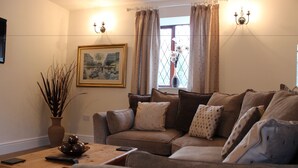 A living room with a sofa, a coffee table, a vase with branches, and a painting on the wall. - Bridge Farm Hotel (Leeds)