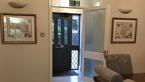 A hallway with a door leading to a dark room, two framed maps on the walls, and a chair in the foreground. - Bridge Farm Hotel (Leeds)