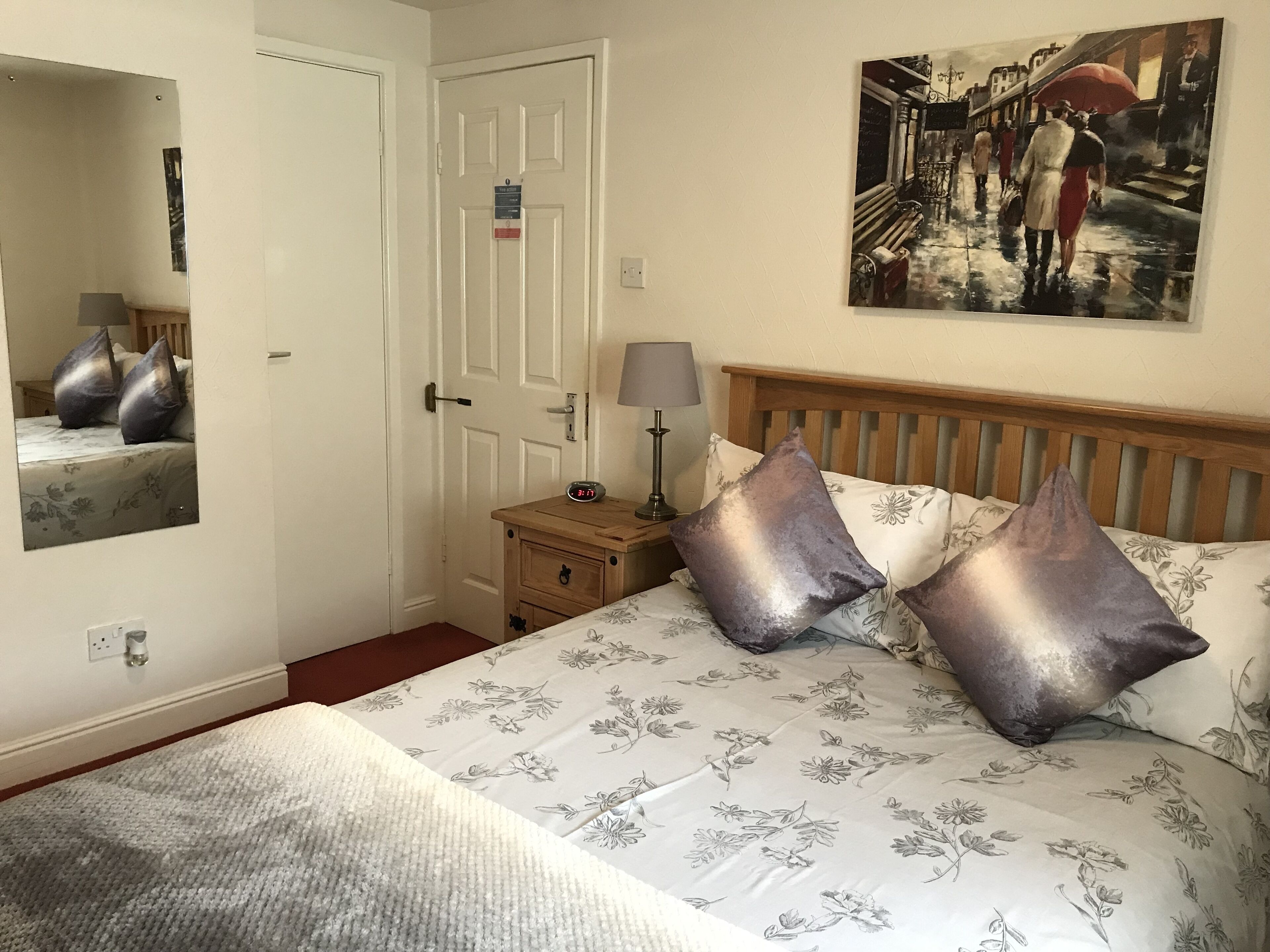 Ein Schlafzimmer mit Bett, Nachttisch, Spiegel, Tür und einem Bild an der Wand.