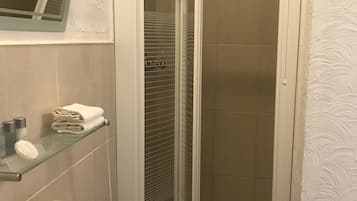A bathroom with a glass-enclosed shower, a sink with a mirror above it, and a shelf with toiletries.