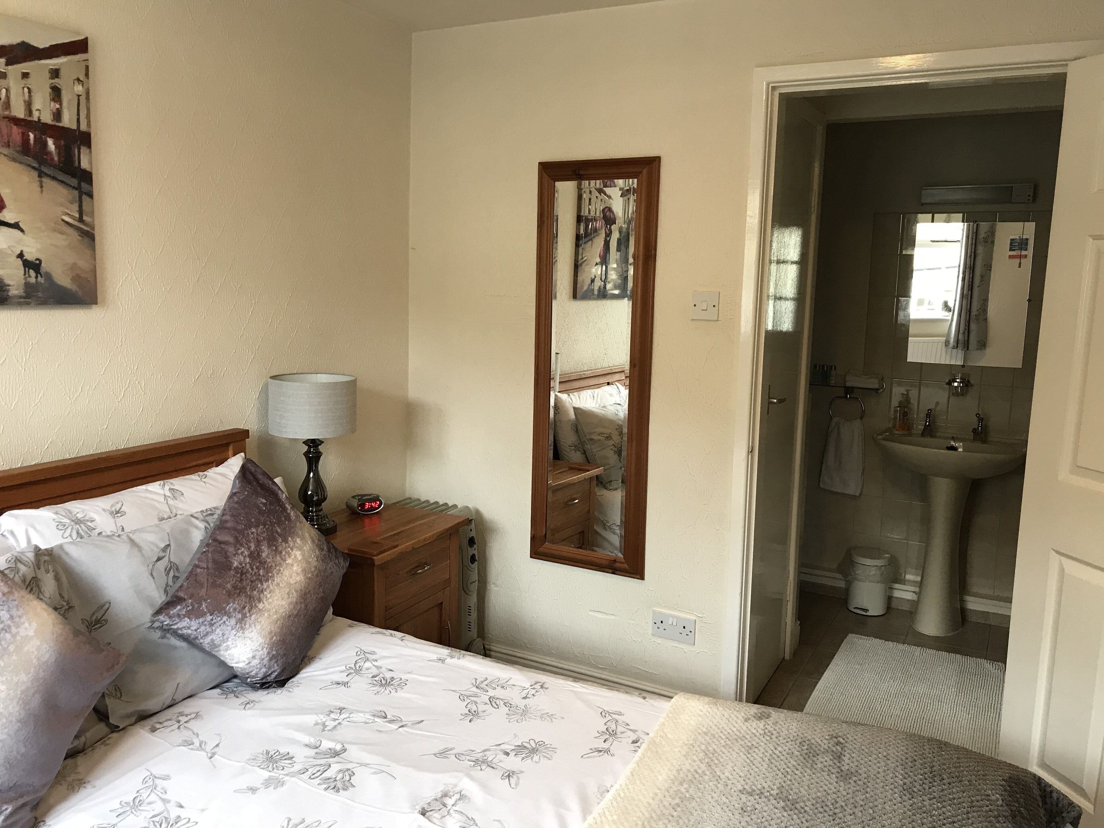 A bedroom with a bed, bedside table, lamp, and a mirror.