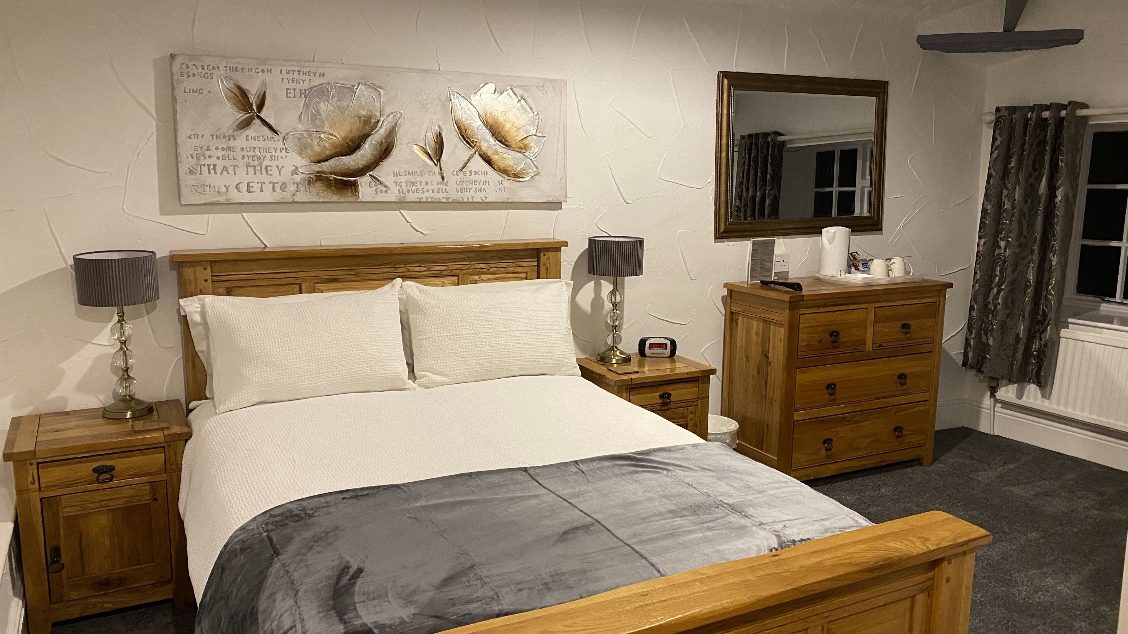 Un dormitorio con una cama de madera, dos mesitas de noche con lámparas, un aparador, un espejo y un adorno en la pared.