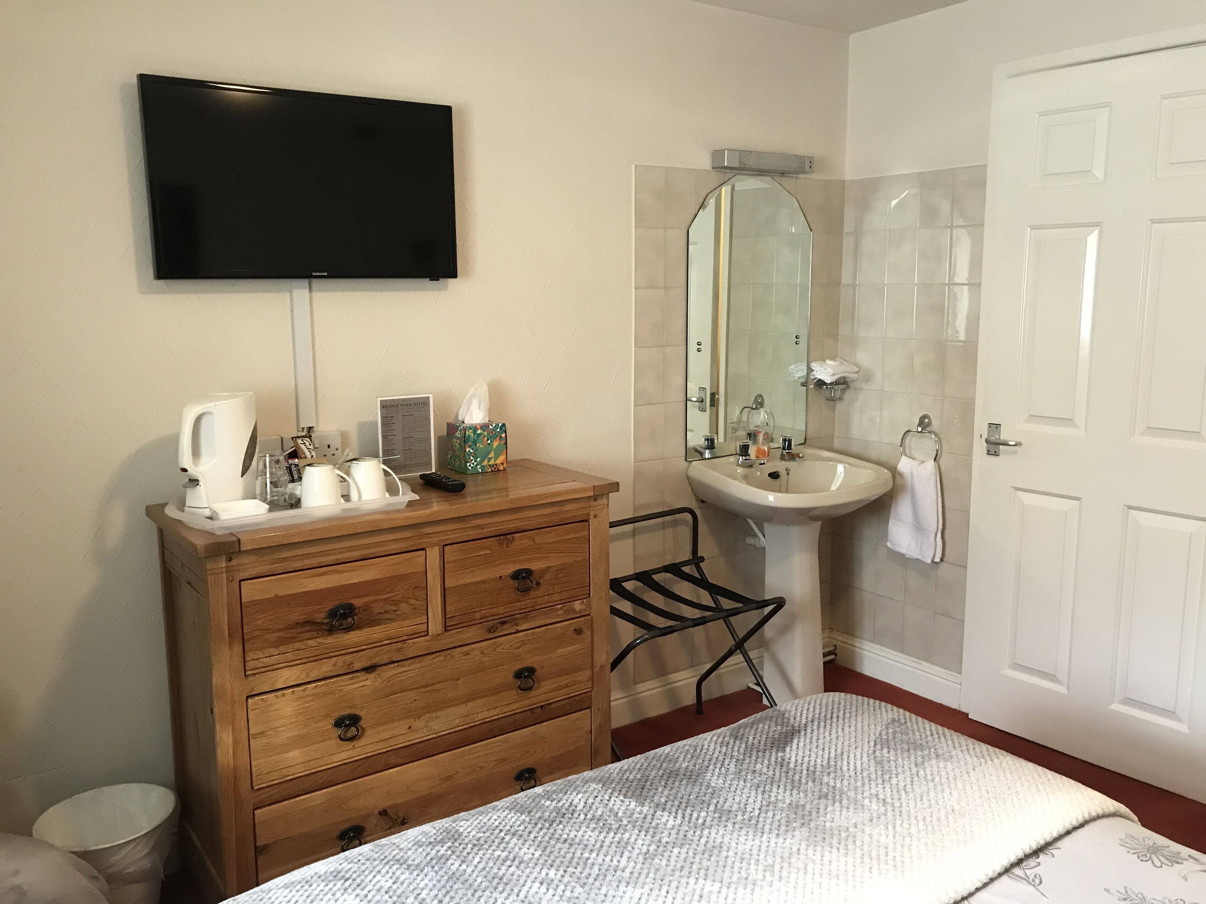 A bathroom with a wooden vanity, a sink, a mirror, a toilet, and a television mounted on the wall.