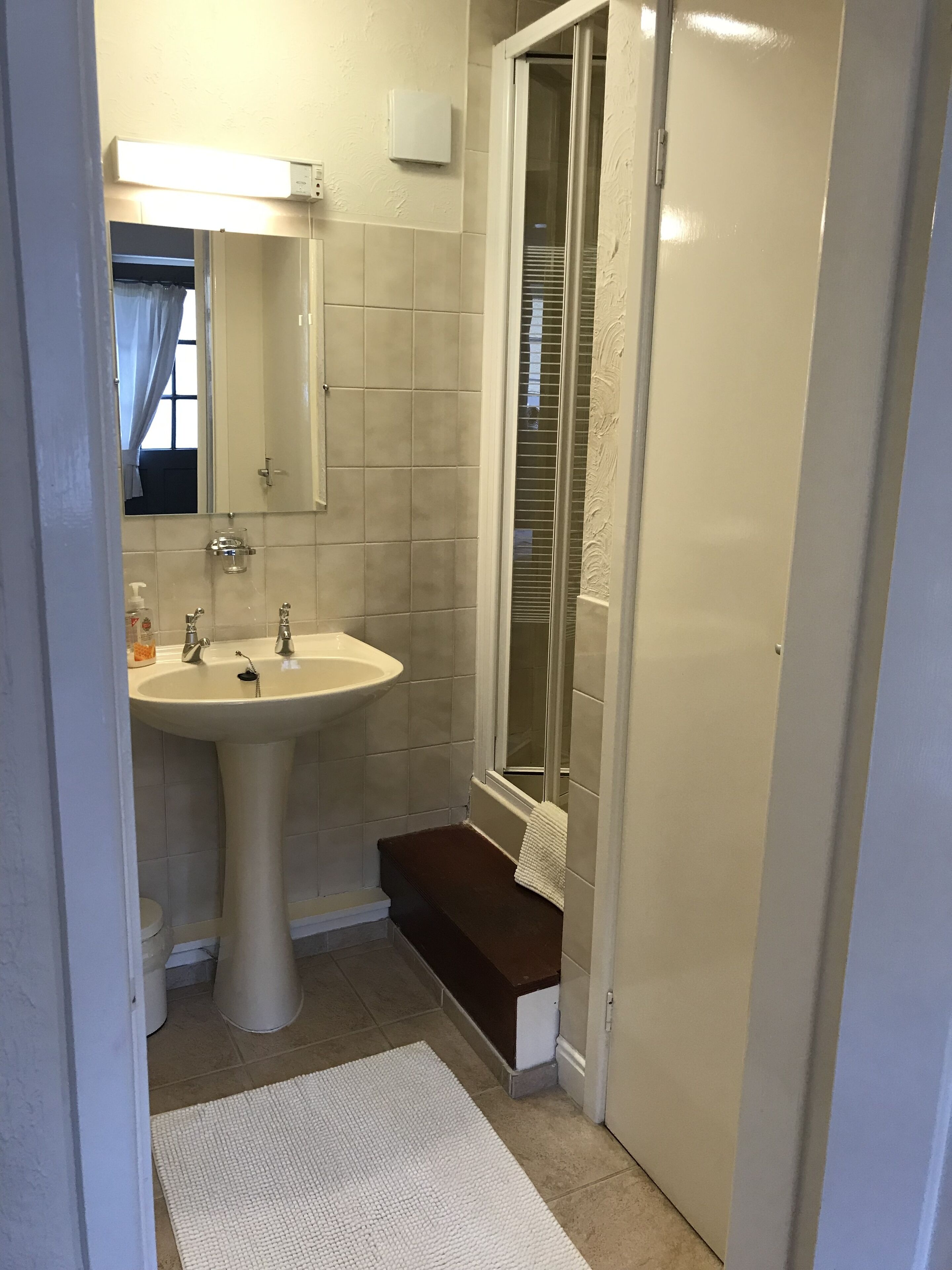 A bathroom with a pedestal sink, a mirror, a towel rack, and a shower area.