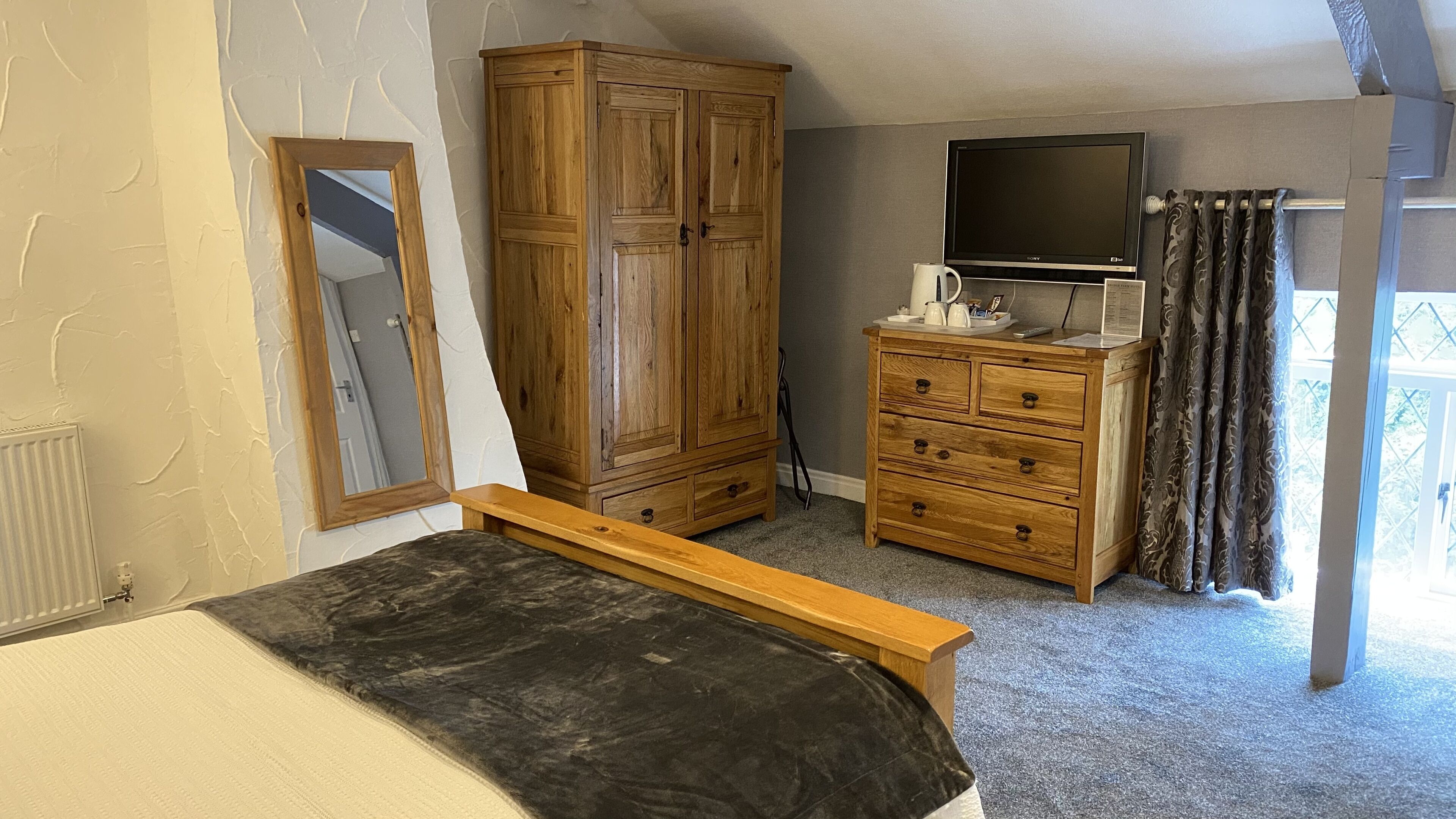 A bedroom with a wooden wardrobe, a television, a bed, and a window with curtains.