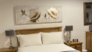 A bedroom with a wooden bed, two bedside tables, a nightstand, a mirror, and a wall-mounted artwork. - Bridge Farm Hotel (Leeds)