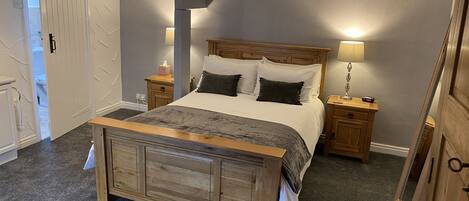 A bedroom with a wooden bed, two bedside tables, a nightstand, and a lamp.
