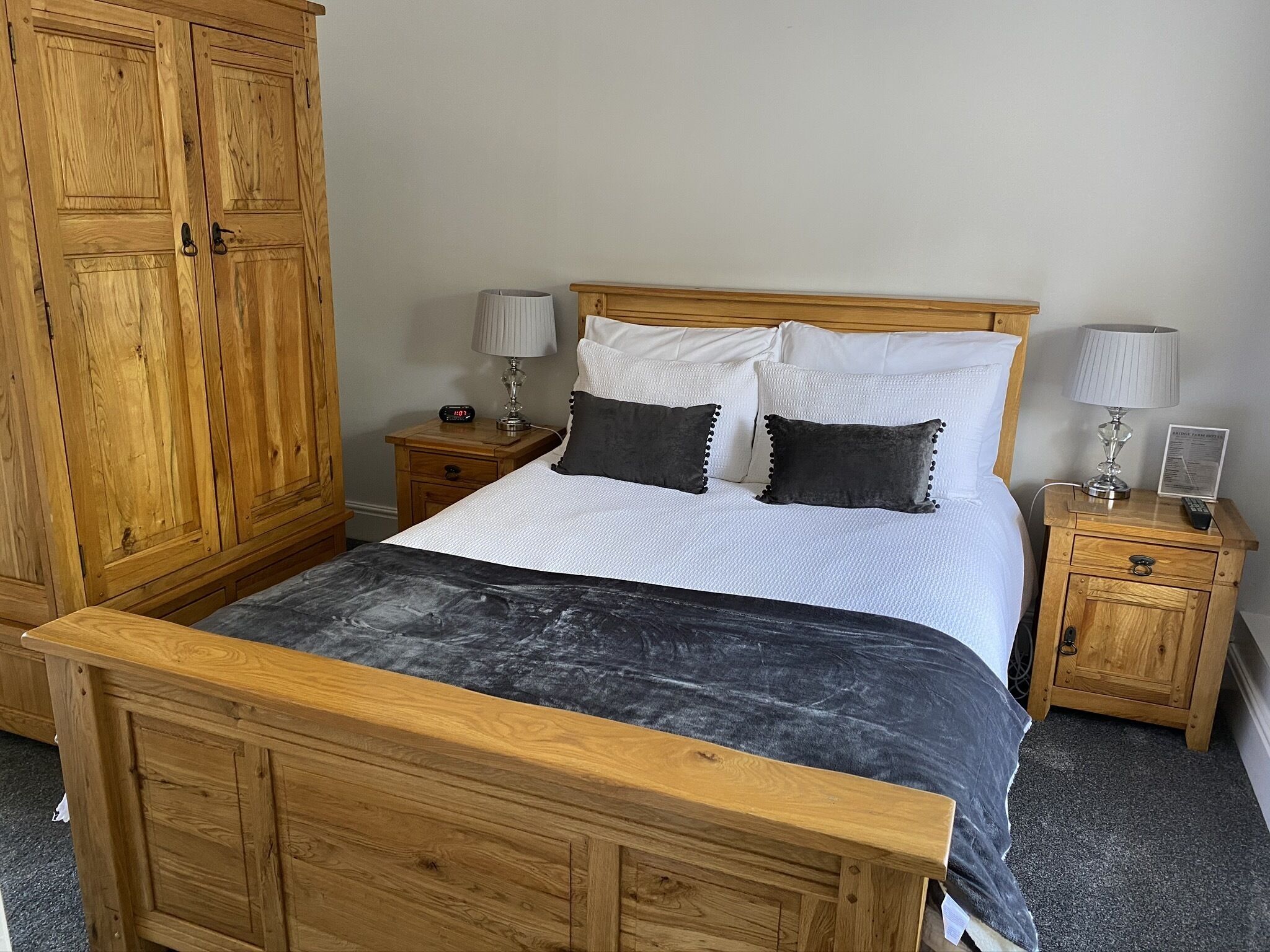 A wooden bed with a white and black bedspread, two bedside tables with lamps, and a wooden wardrobe.