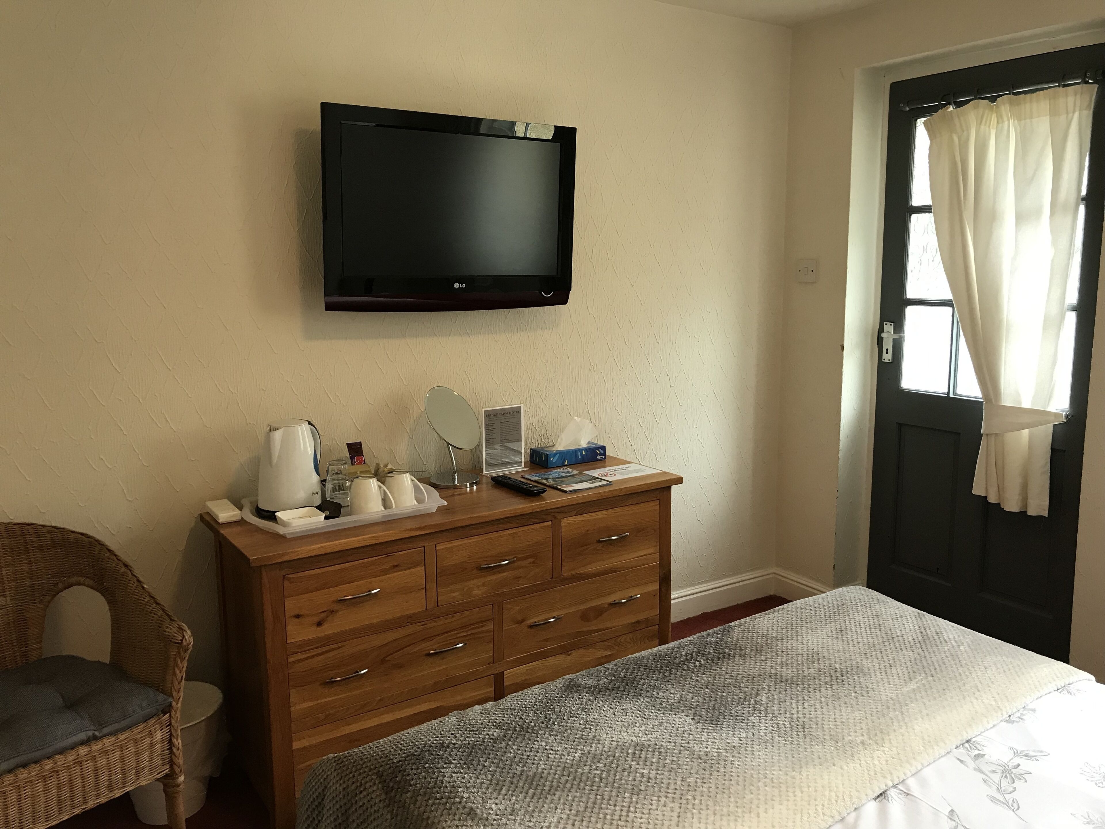 A bedroom with a bed, wooden dresser, and a flat-screen TV mounted on the wall.