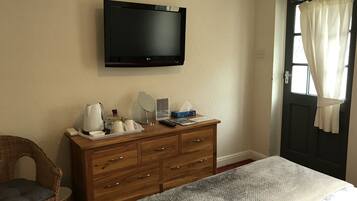 A bedroom with a bed, wooden dresser, and a flat-screen TV mounted on the wall.