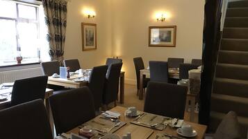 A dining area with tables set for breakfast, featuring a menu, cutlery, and a coffee pot.