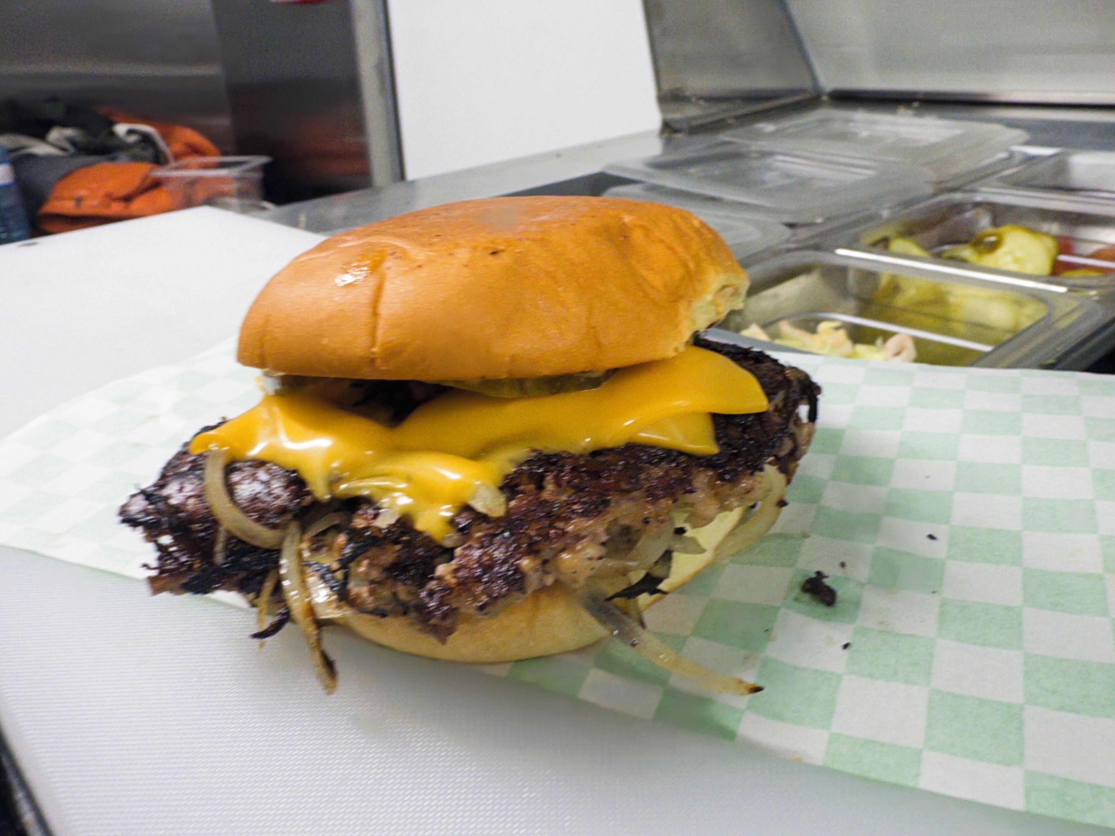 A burger with a bun, cheese, and onions on a checkered paper.