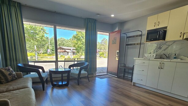 A spacious living area with a sofa, dining table, and chairs, a kitchen with a microwave and sink, and large windows offering a view of the outdoors. - Arrowhead Inn by Baaman's (Huntsville)
