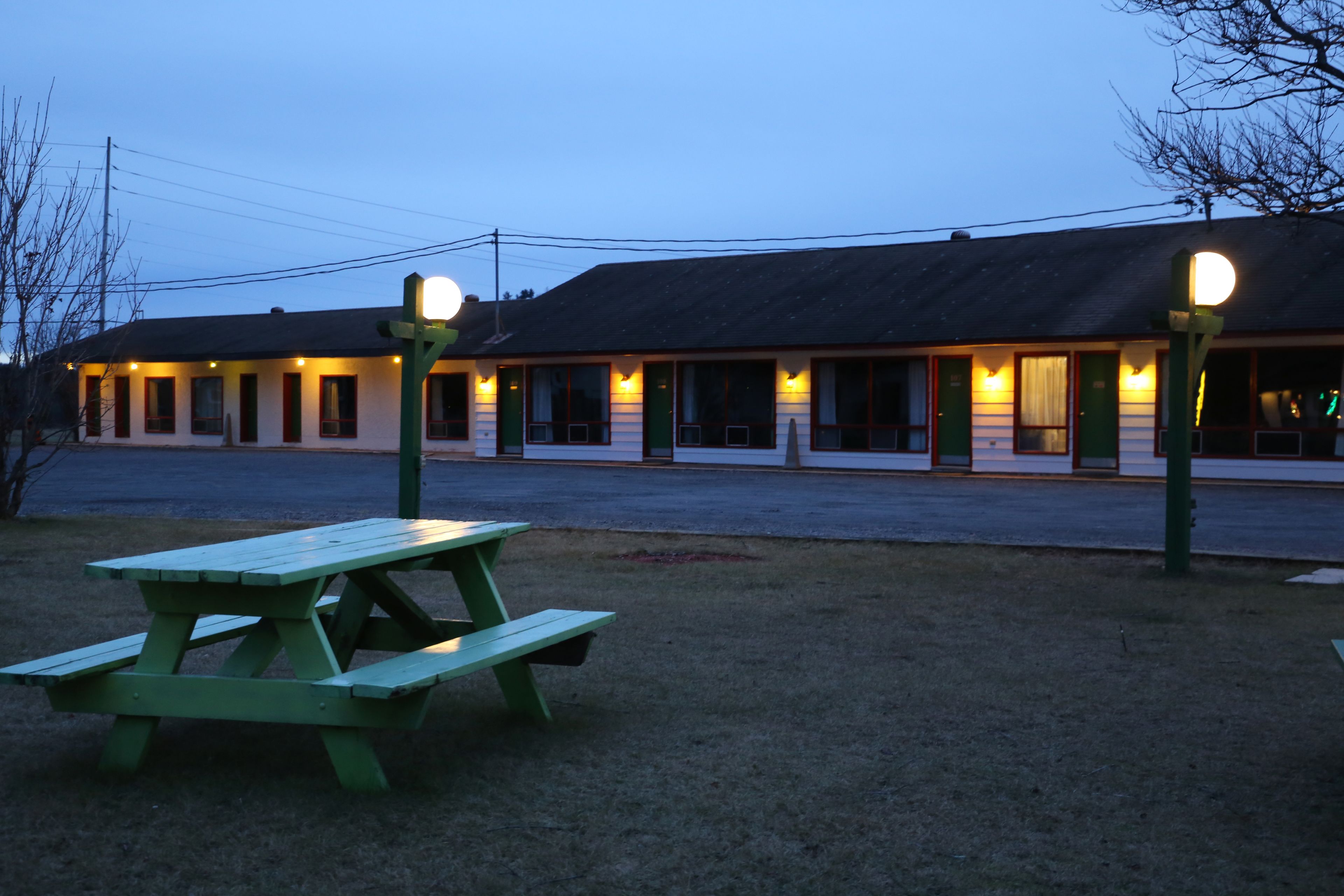 A motel with a row of rooms, a picnic table, and street lamps.