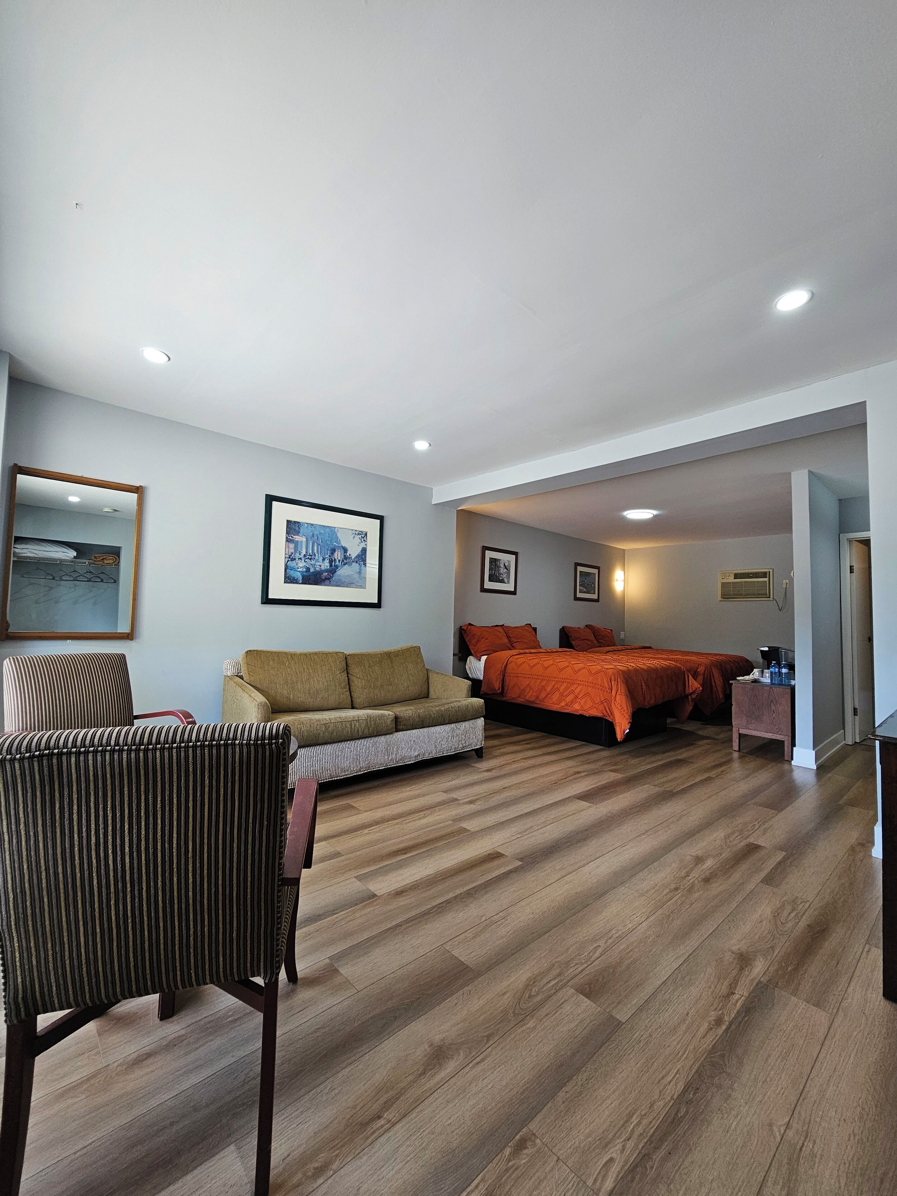 A hotel room with a sofa, a bed with orange bedding, a striped chair, and a framed picture on the wall.
