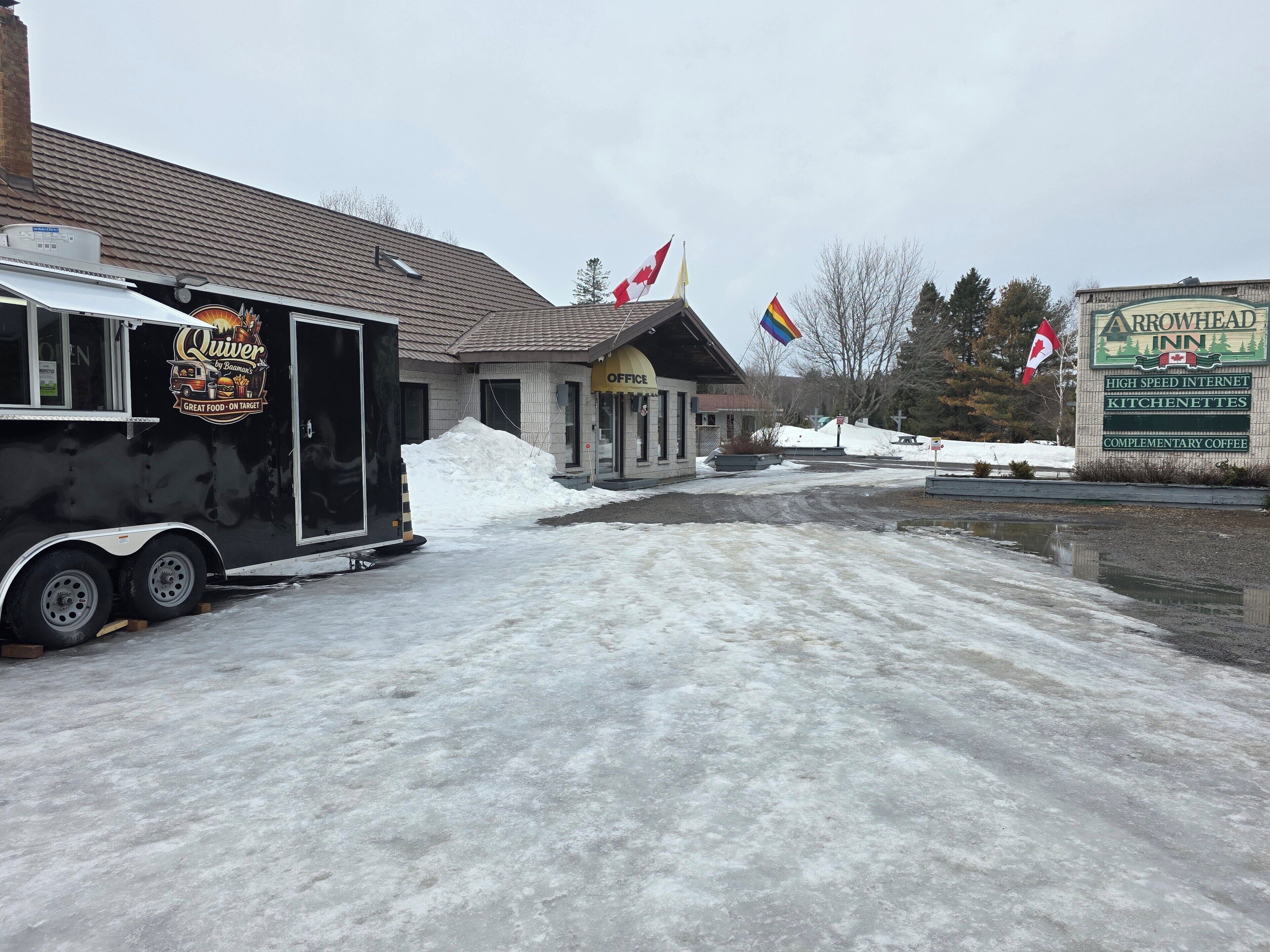 A building with a sign for Arrowhead Inn, a snow-covered parking lot, and a food truck with a logo.