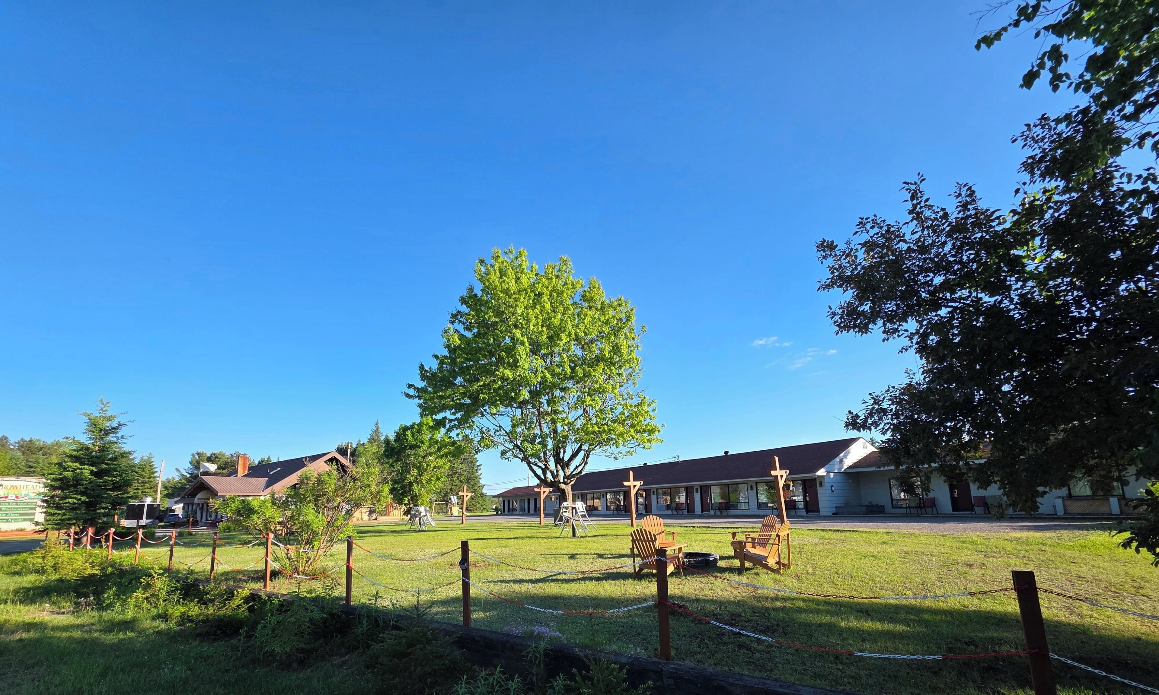 A grassy area with a large tree, a playground, and a building with a red roof.