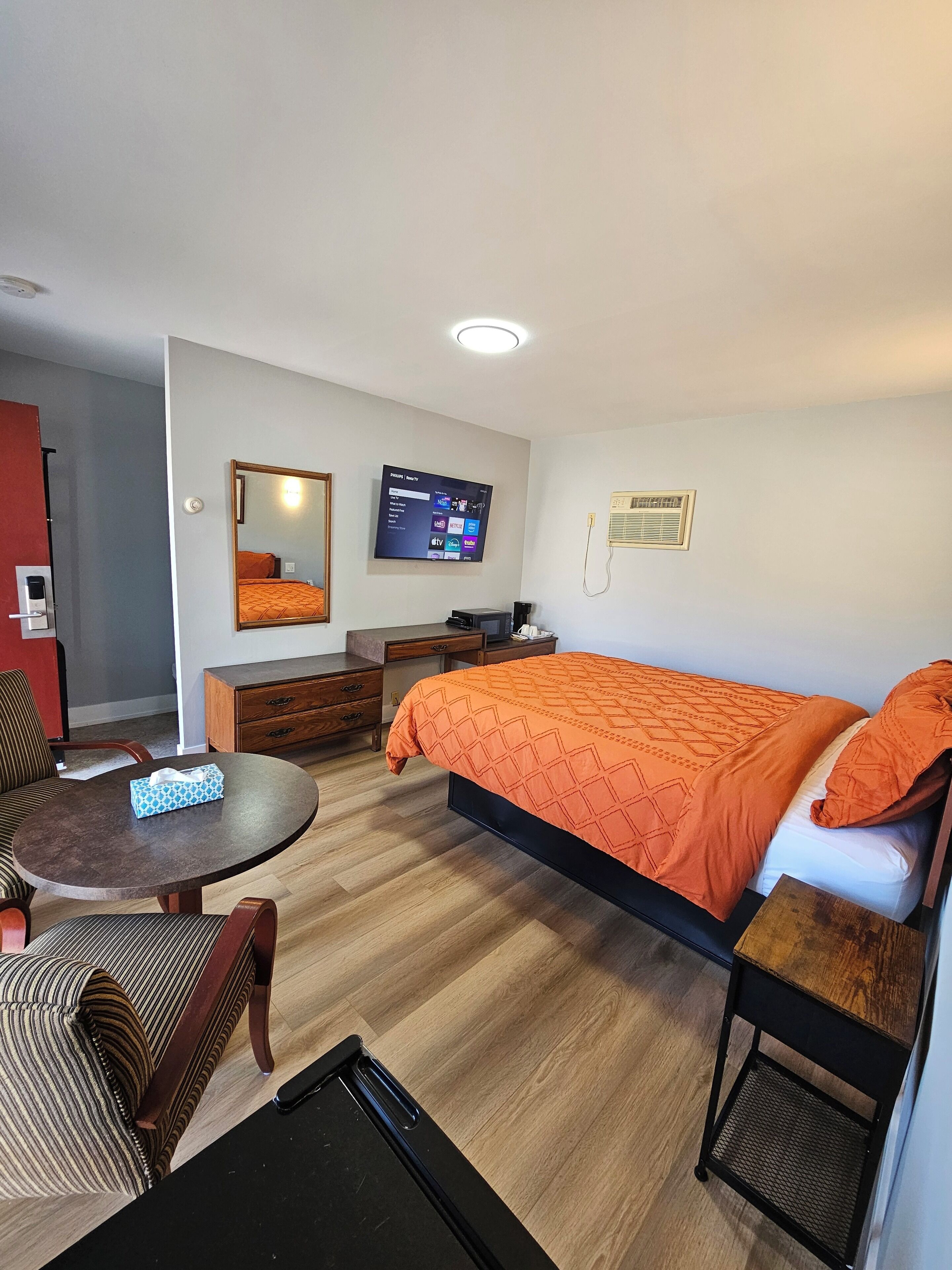 A hotel room with a bed, a desk, a chair, a TV, and a small table.