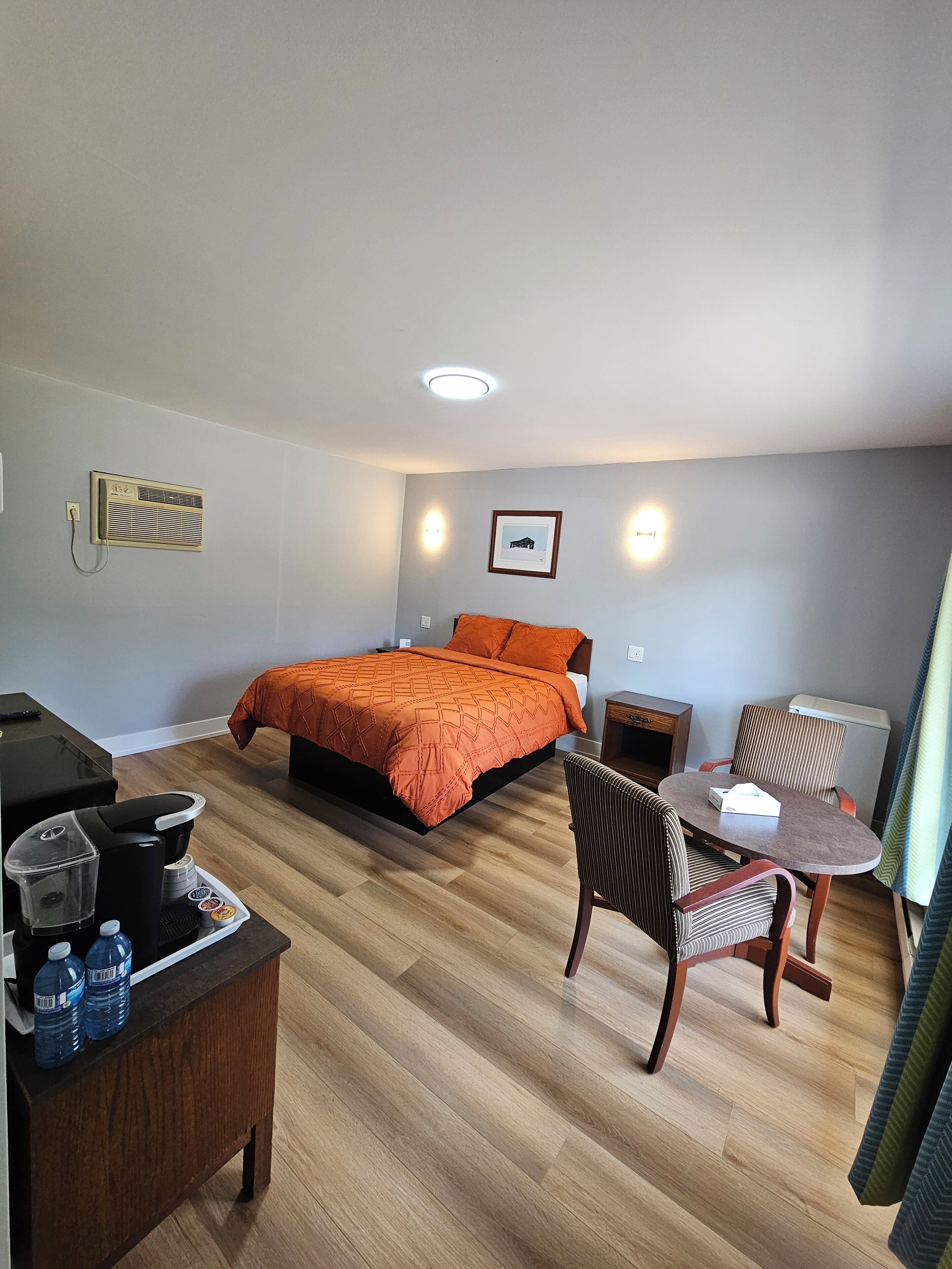 A hotel room with a bed, a desk with a coffee maker, a chair, and a table.