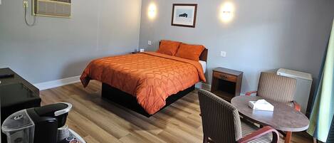 A hotel room with a bed, a desk with a coffee maker, a chair, and a table.