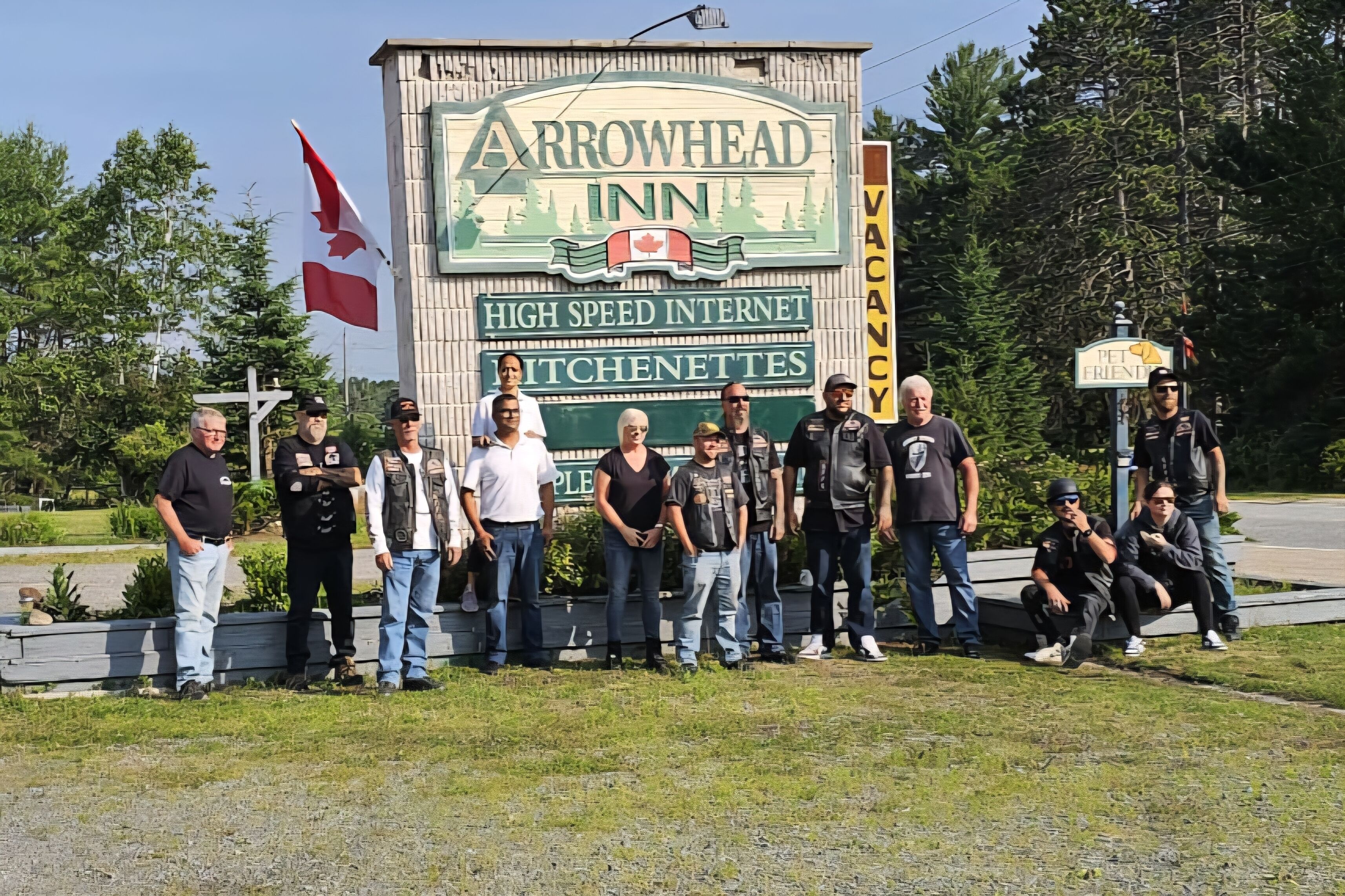 Un groupe de personnes se tient devant l’enseigne de l’hôtel Arrowhead Inn, sur laquelle on peut lire les mentions « Internet haut débit » et « cuisinettes ».