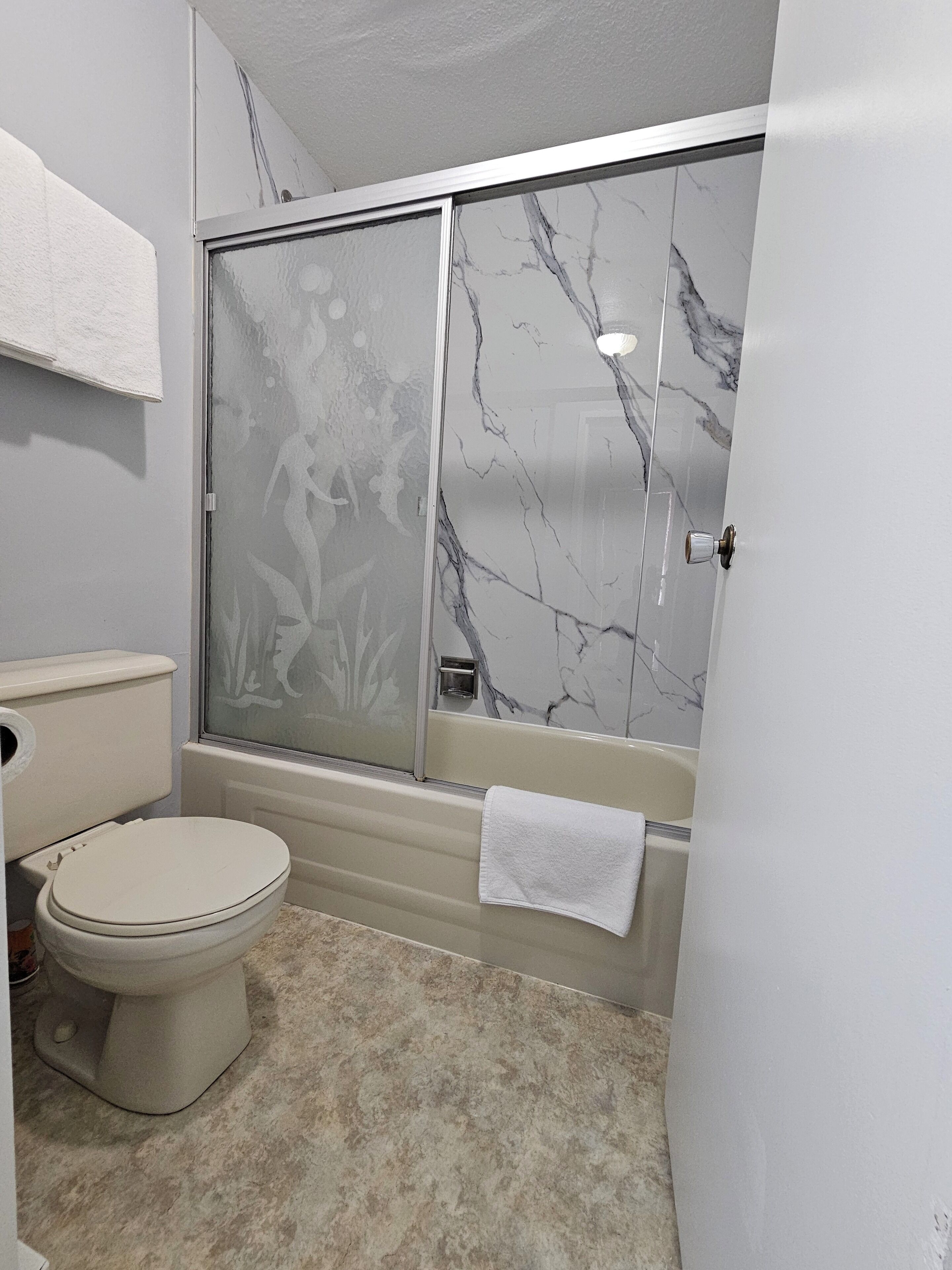 Une salle de bain avec des toilettes, une douche aux murs en marbre et une serviette accrochée au mur.