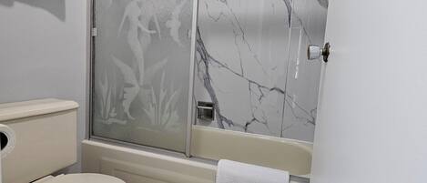 A bathroom with a toilet, a shower with marble walls, and a towel hanging on the wall.