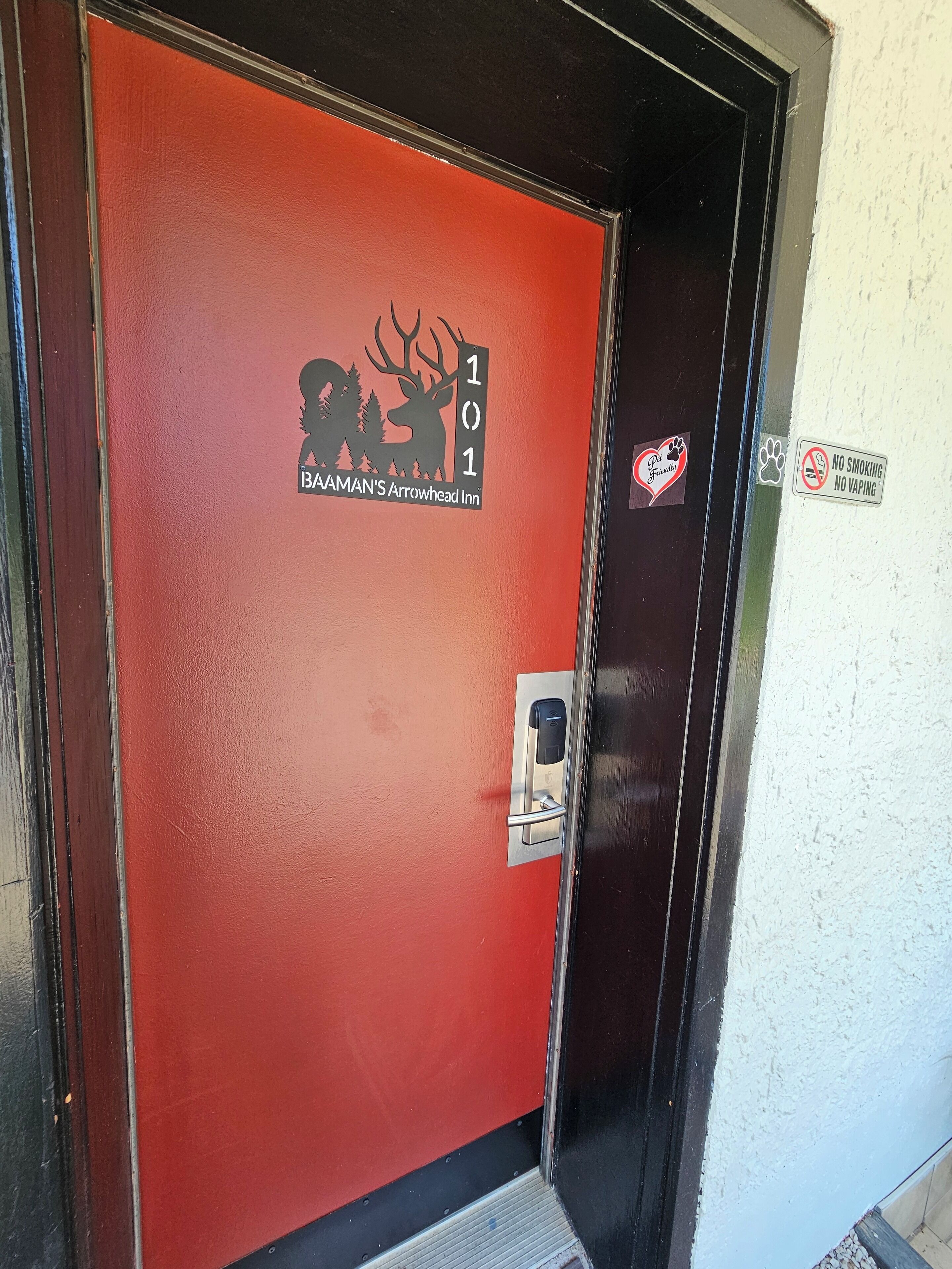 Uma porta vermelha com o logotipo do Baaman's Arrowhead Inn, uma placa indicando proibido fumar e uma placa informando que aceita animais de estimação.