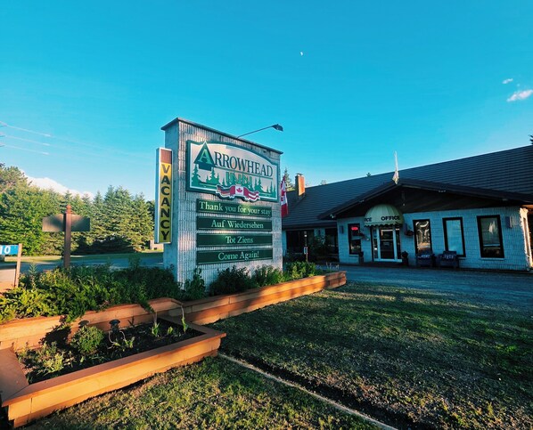 A signboard for Arrowhead Inn with multilingual greetings and a small building with an 'Office' sign.