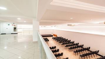A spacious, well-lit conference room with rows of black chairs, a white reception desk, and a tiled floor.