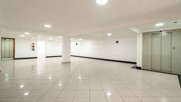 A spacious, well-lit hallway with a tiled floor, a fire extinguisher, and an elevator.