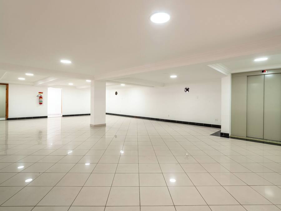 A spacious, well-lit hallway with a tiled floor, a fire extinguisher, and an elevator.