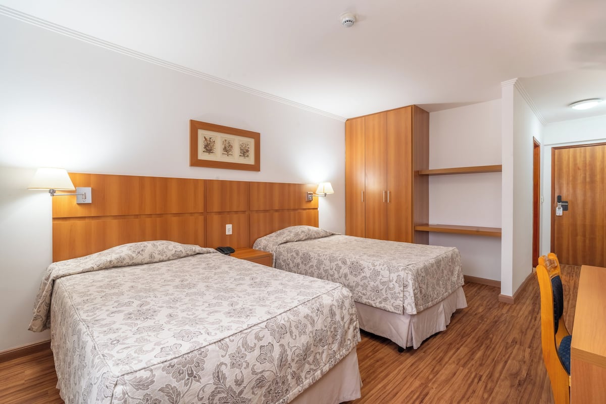 Habitación de hotel con dos camas, cabecero de madera, un armario de madera y un escritorio con una silla.