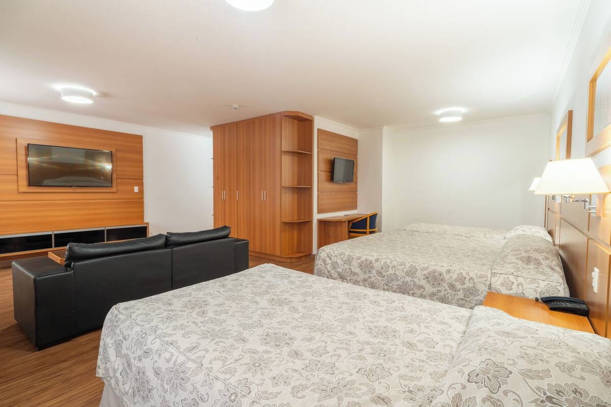 Habitación de hotel con dos camas, un sofá, un televisor y un armario de madera.