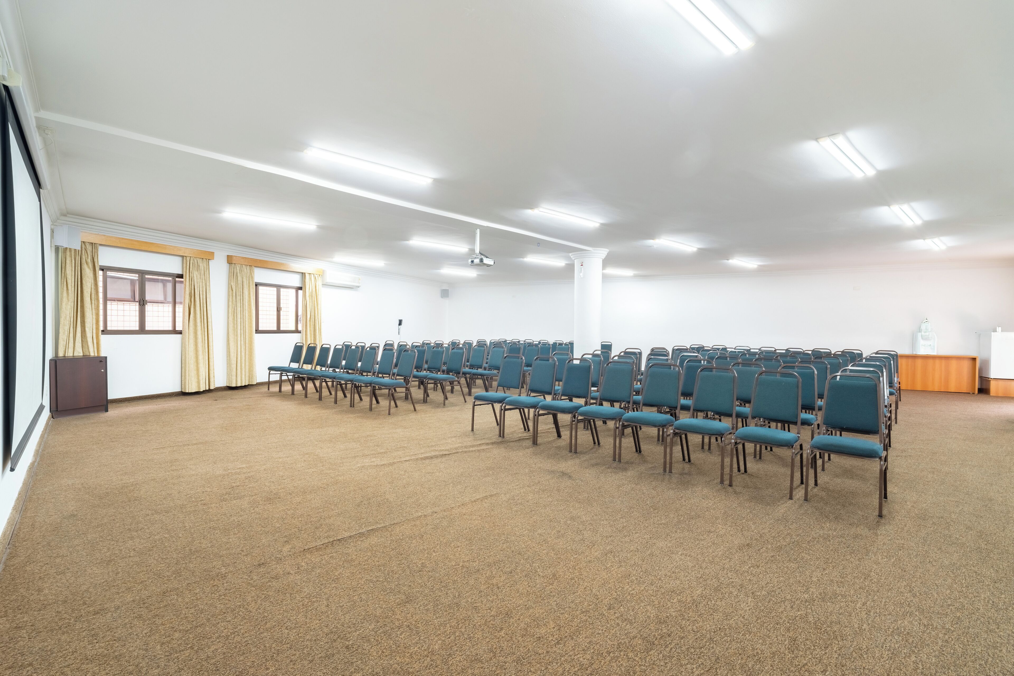 Un salón de conferencias con filas de sillas, un proyector y un atril.