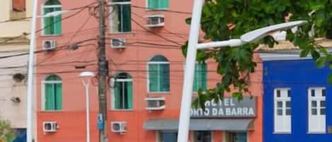 A multi-story building with a red facade and a blue door. There are air conditioning units on the windows, and a sign that reads "EL DOMO DA BARRA".