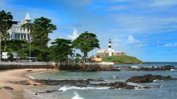 Uma paisagem costeira com um farol, um edifício grande e uma praia.